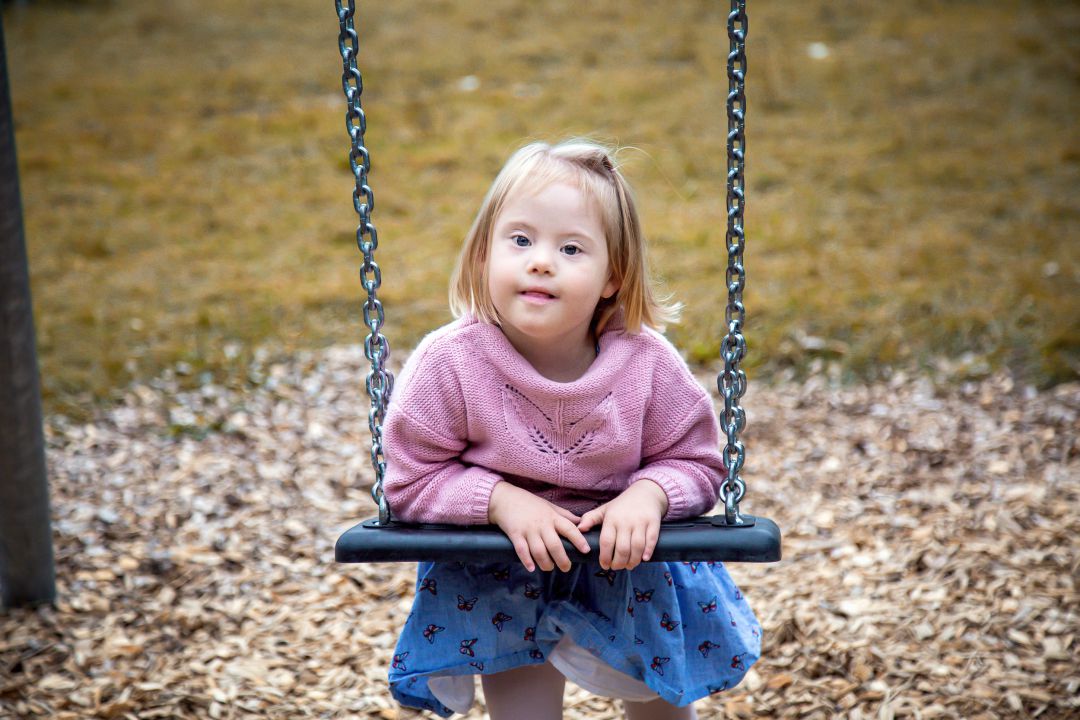 Kind, dass auf eine Schaukel gestützt in die Kamera blickt