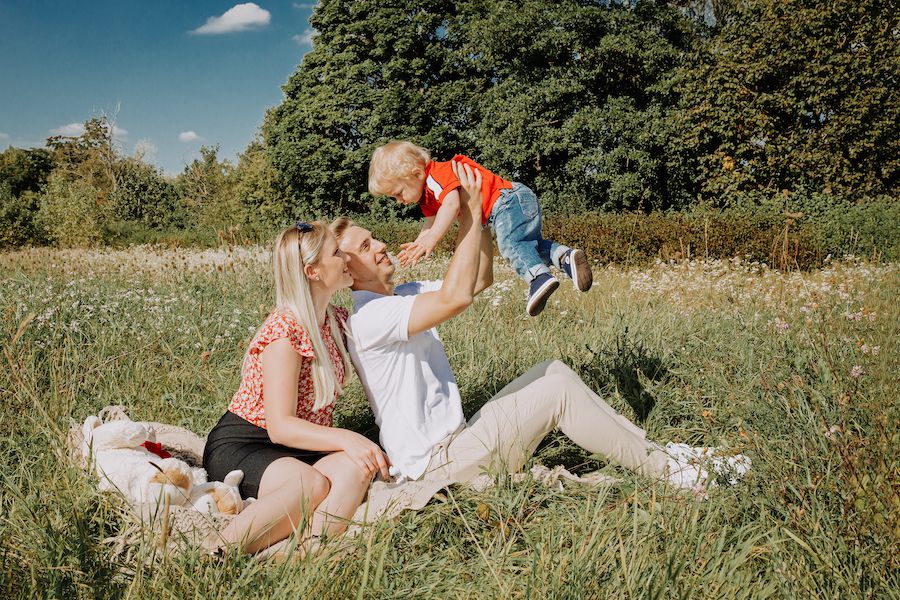 Junge Familie auf einer Wiese, die ihr Kind in die Luft hebt