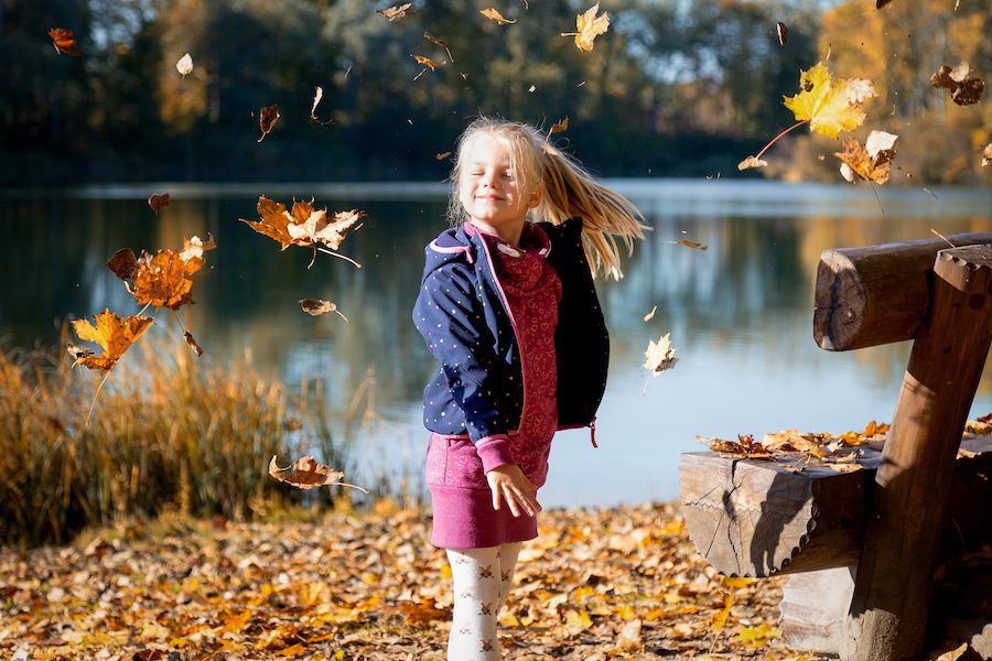 Kind vor einem See mit Herbstblättern im Wind